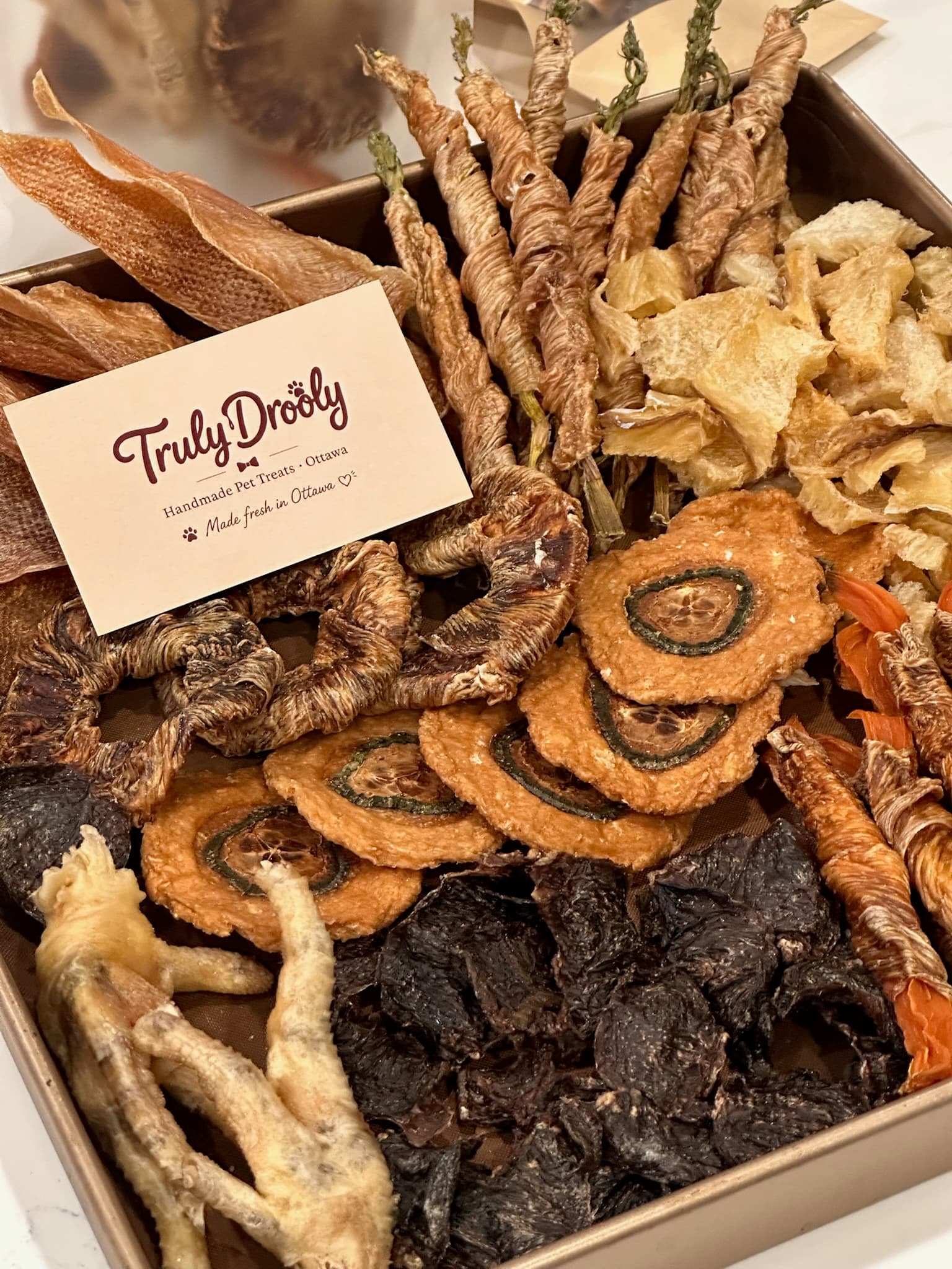 A handmade Truly Drooly tray filled with slow-dried meat treats and a kraft brand card
